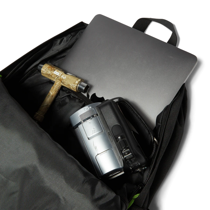 Black backpack with a silver laptop, black camera, and wooden tool on a white background