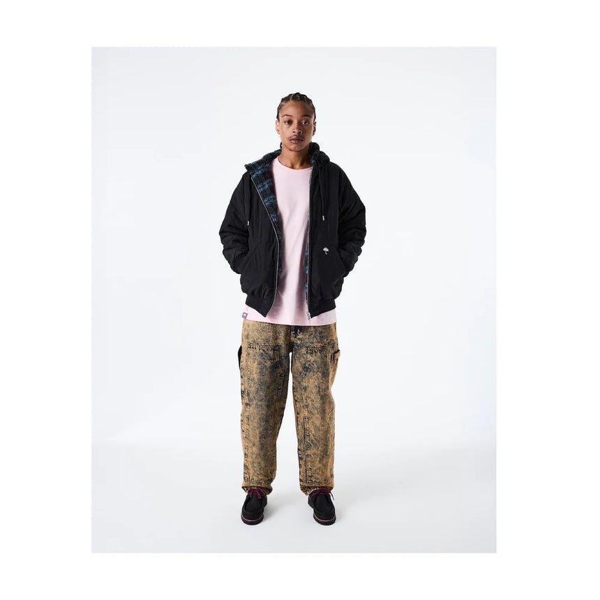 Person wearing a black jacket, pink shirt, and patterned pants on a white background