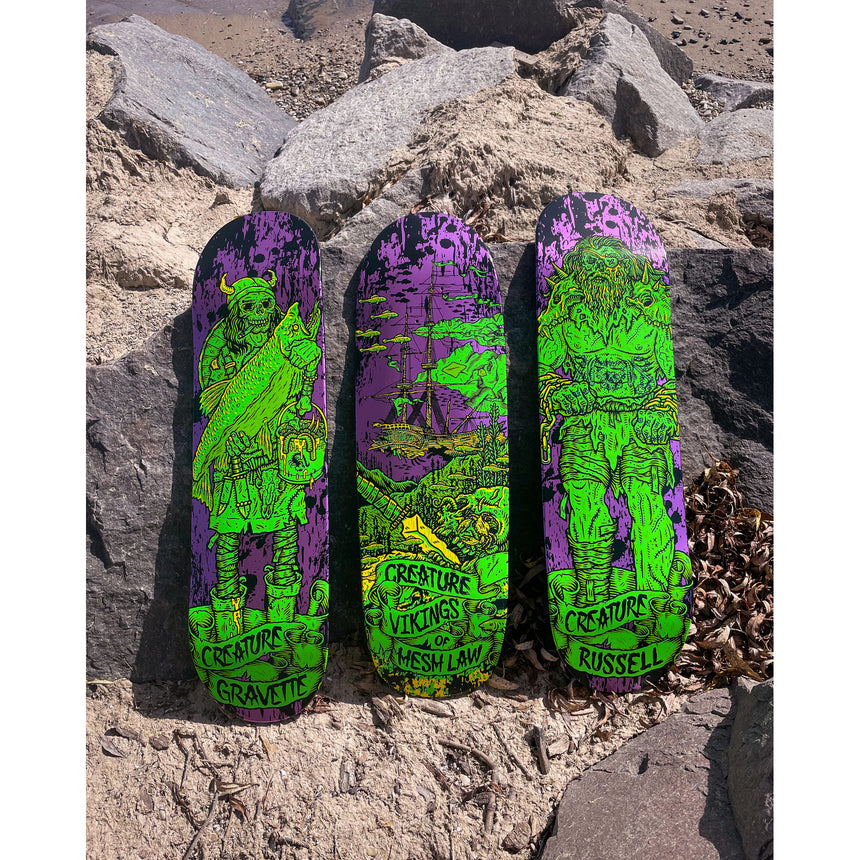 Three skateboard decks with green and purple designs on a rocky surface