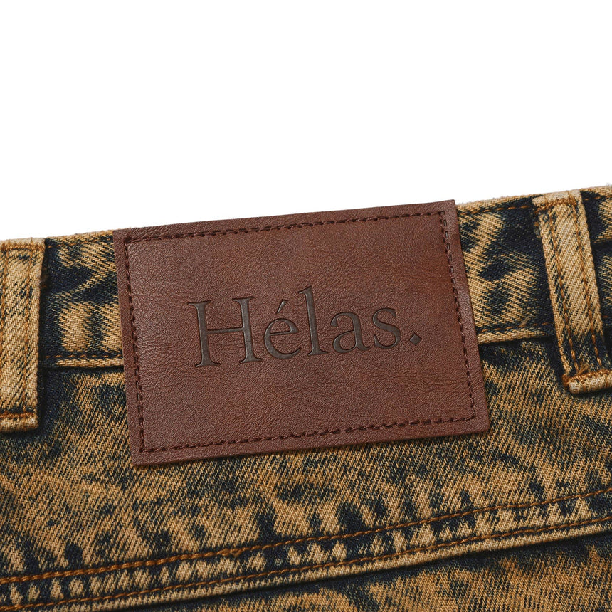 Close-up of a brown leather patch with 'Hélas' branding on a patterned fabric background.