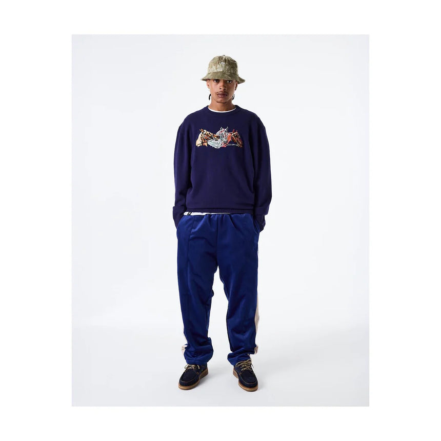 Person wearing a navy sweatshirt with a colorful graphic and blue pants on a white background