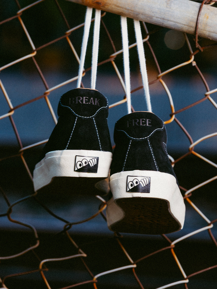 Black sneakers with white soles hanging on a chain-link fence.