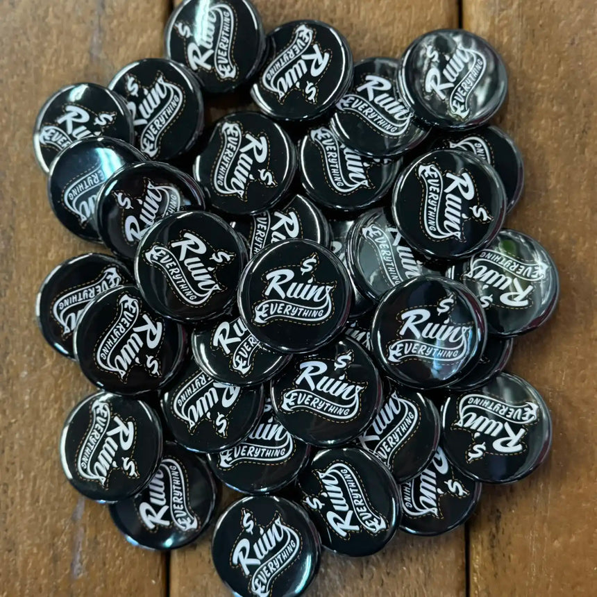 Collection of black buttons with 'Ruins Everything' text on a wooden surface