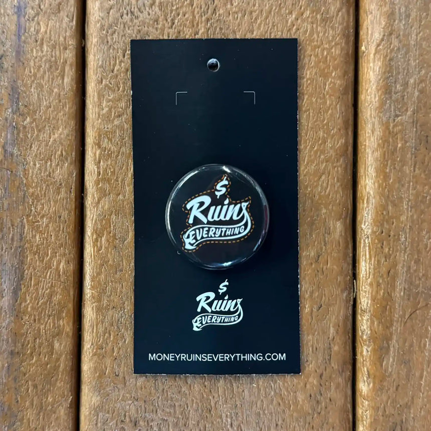 Button badge with 'Ruins Everything' text on a black card against a wooden background