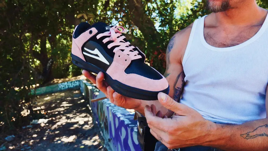 Person holding a black and pink sneaker outdoors with greenery in the background
