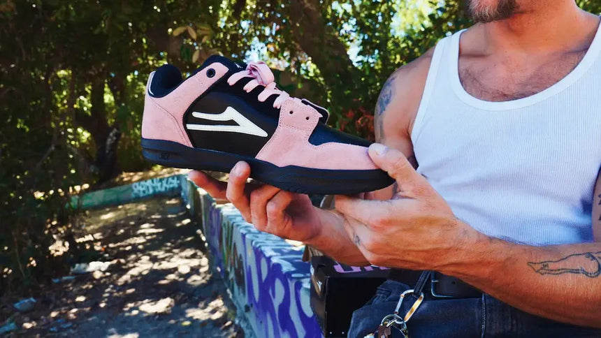 Person holding a pink and black sneaker outdoors with greenery in the background
