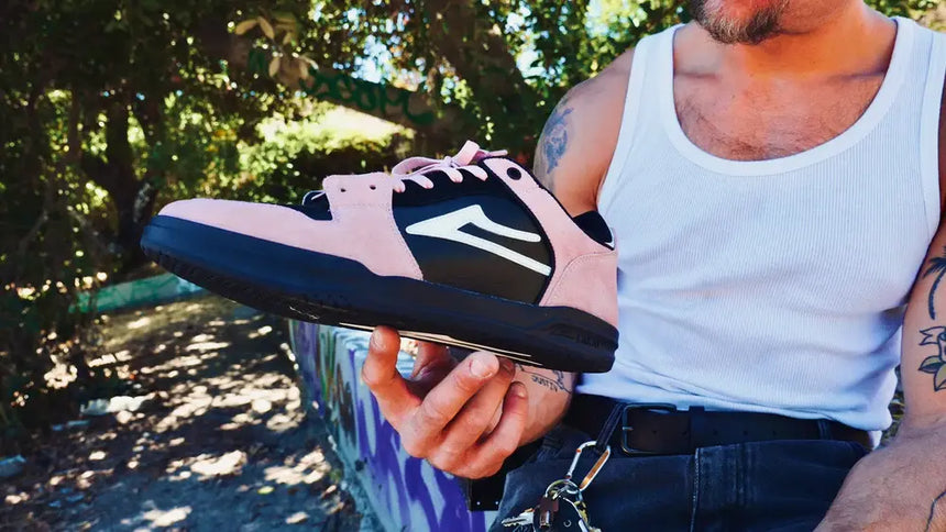 Person holding a black and pink sneaker with a brand logo outdoors.