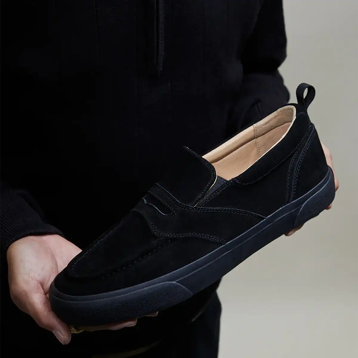 Person holding a black loafer shoe against a neutral background