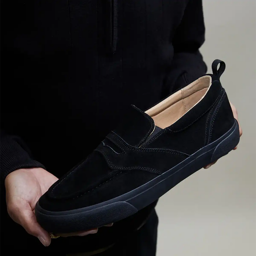 Person holding a black loafer shoe against a neutral background