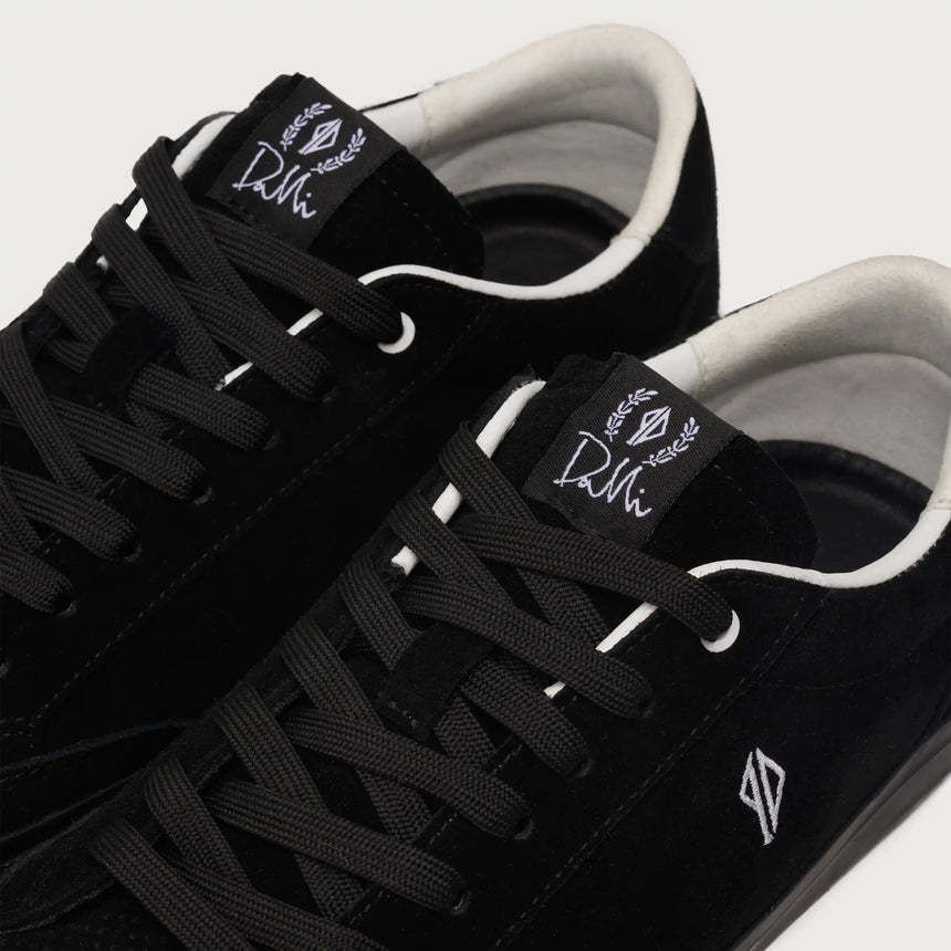 Black sneakers with white soles and visible branding on a light gray background