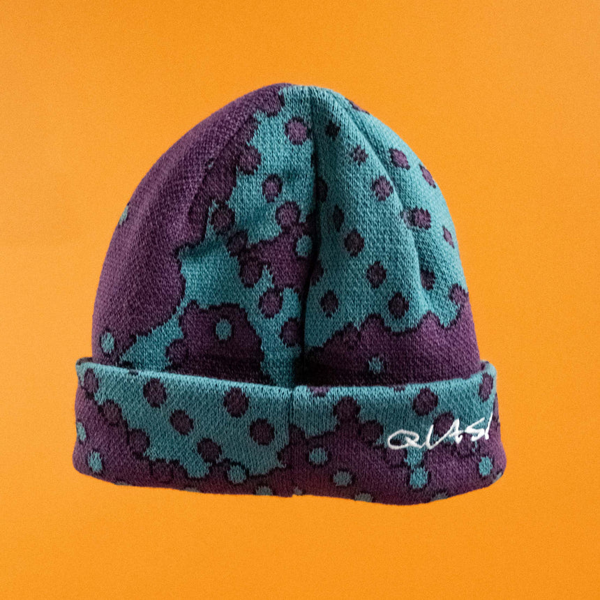 Blue and purple patterned beanie with a brand logo on an orange background