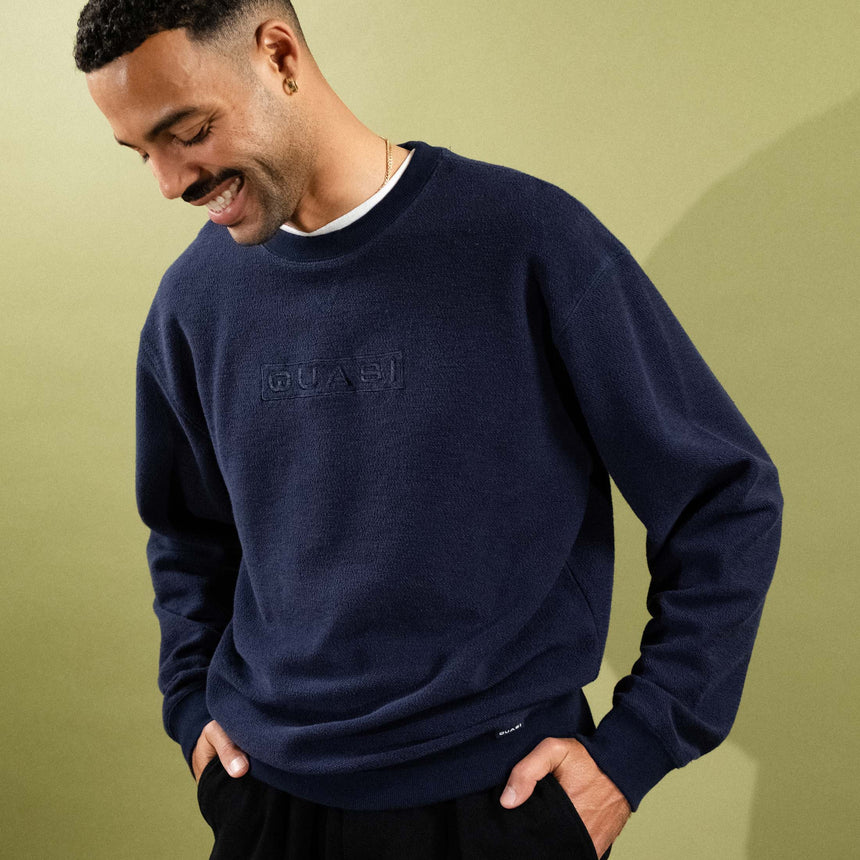 Man wearing a navy blue sweater with a logo on a light green background