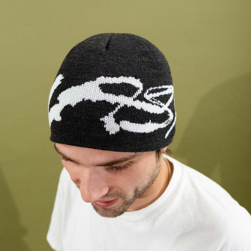 Person wearing a black beanie with a white logo against a green background