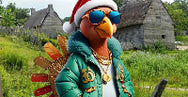 Animated character in a festive outfit with sunglasses and a hat, standing in a grassy area with buildings in the background.