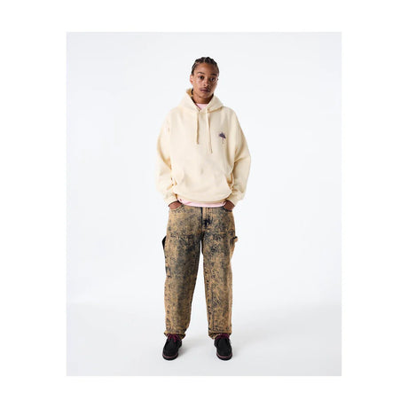 Person wearing a beige hoodie and patterned pants on a white background