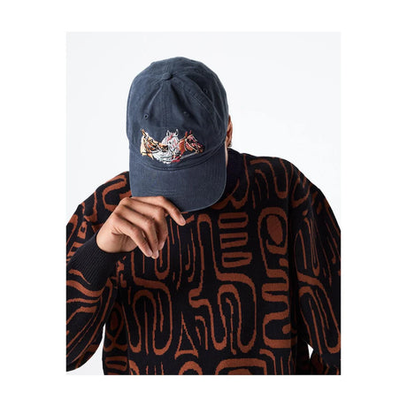 Person wearing a dark blue cap with a colorful design, holding it up to their face on a white background.