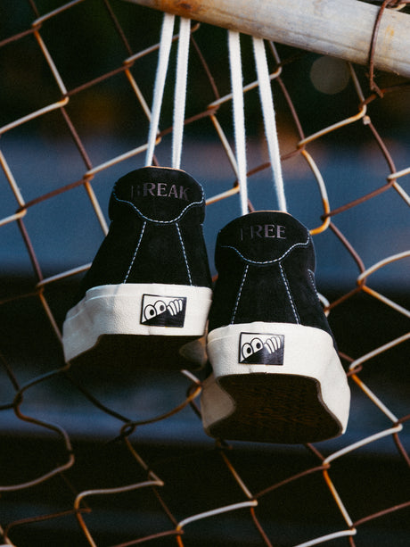Black sneakers with white soles hanging on a chain-link fence.