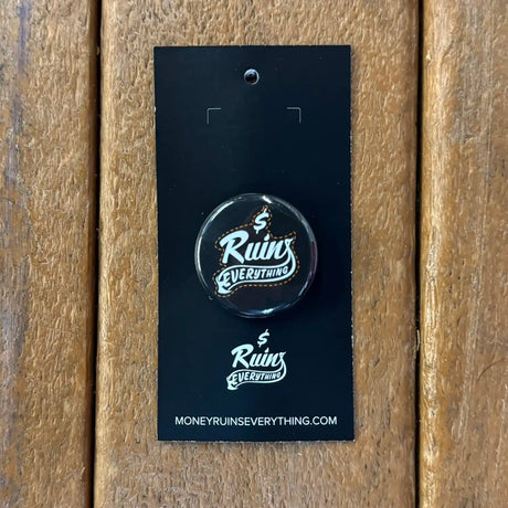 Button badge with 'Ruins Everything' text on a black card against a wooden background
