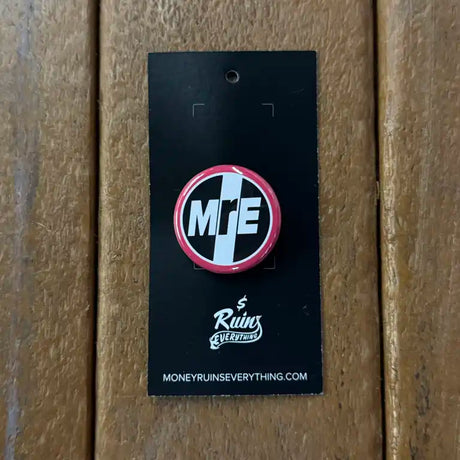 Pin with 'MRE' logo on a black card against a wooden background